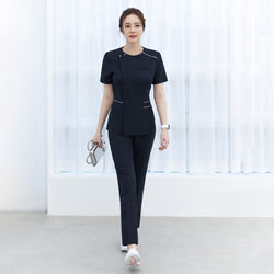 Image of Woman walking in navy side-banding scrub pants with a matching navy top featuring white piping details and short sleeves, showing the full front view,Mir Navy