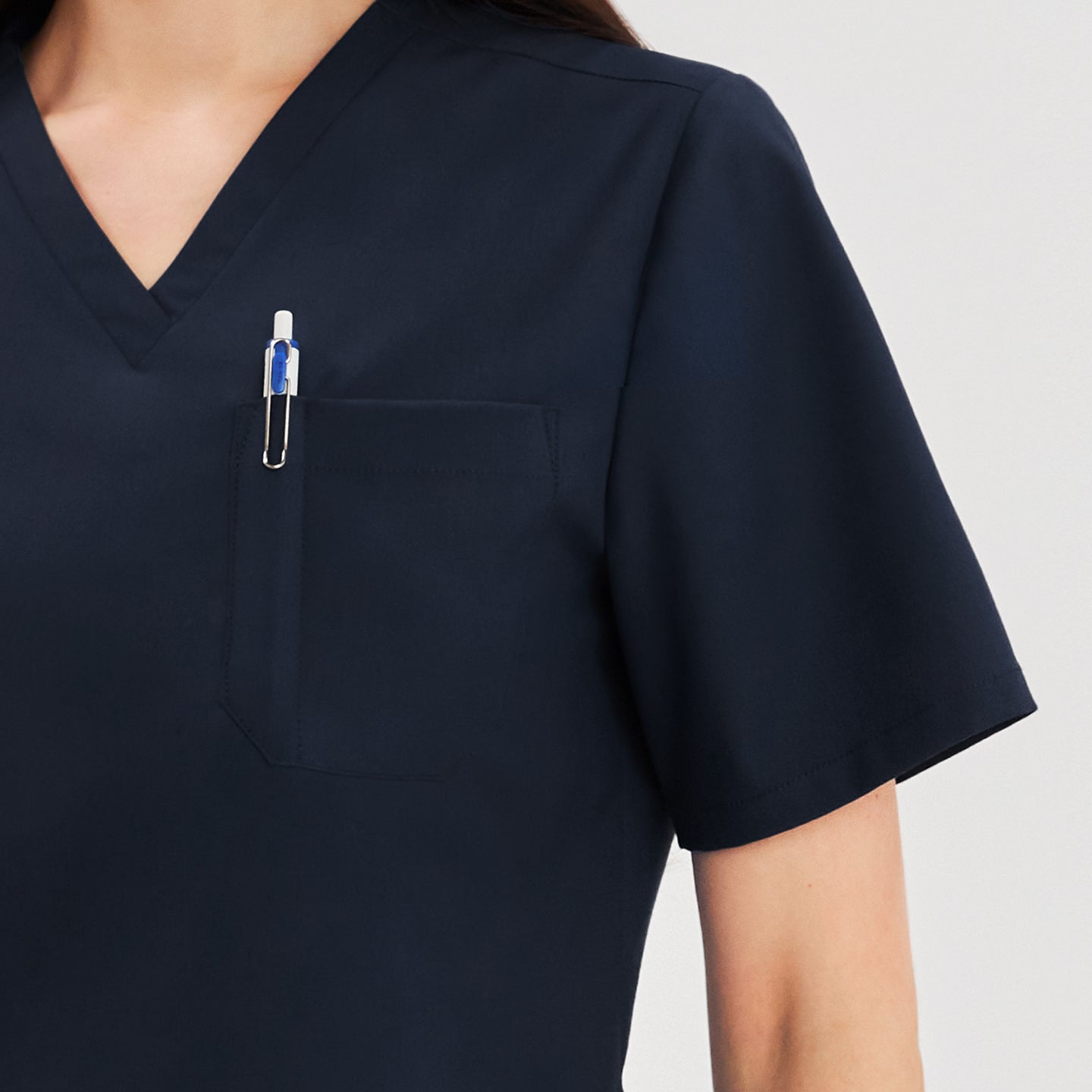 Close-up view of the chest pocket detail on a scrub top, showing a pen placed in the pocket for utility,Navy