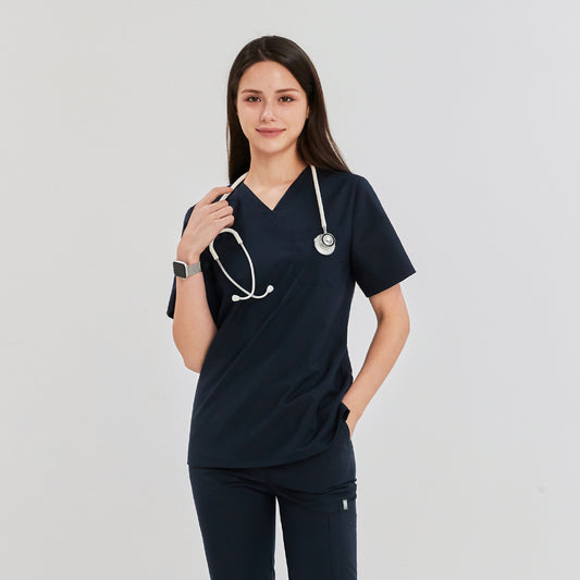 Young woman wearing a scrub top and pants, standing with a stethoscope around her neck and one hand in her pocket, looking confidently at the camera Navy