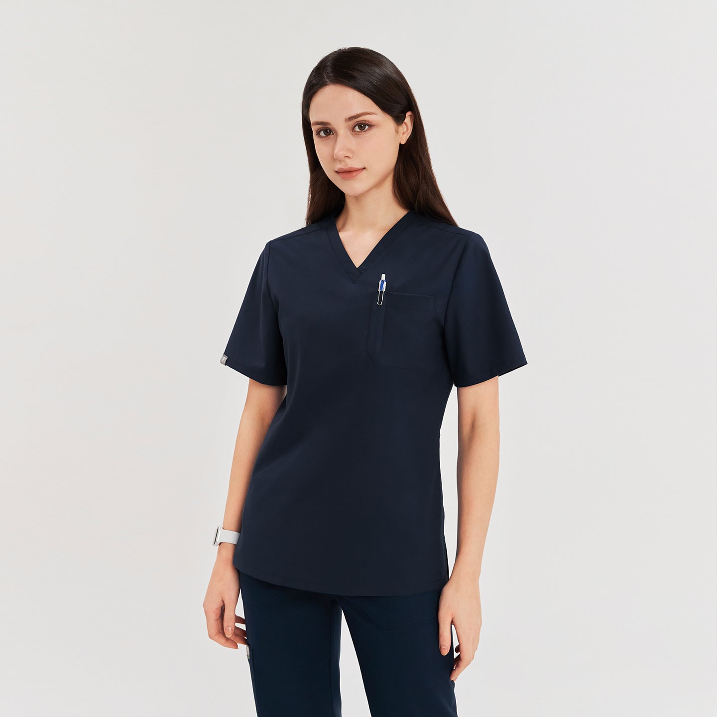 Female model wearing a navy 3-pocket scrub top with a pen in the chest pocket, providing a sleek and functional uniform for medical professionals,Navy