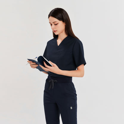 Female model wearing a navy 3-pocket scrub top and matching pants, holding a notebook and pen, suitable for healthcare professionals,Navy