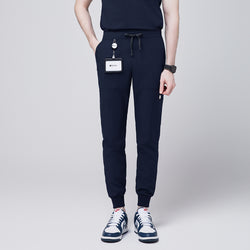 Image of Front view of navy 8-pocket jogger scrub pants with drawstring waistband, cuffed ankles, and a name badge, paired with sneakers,Navy