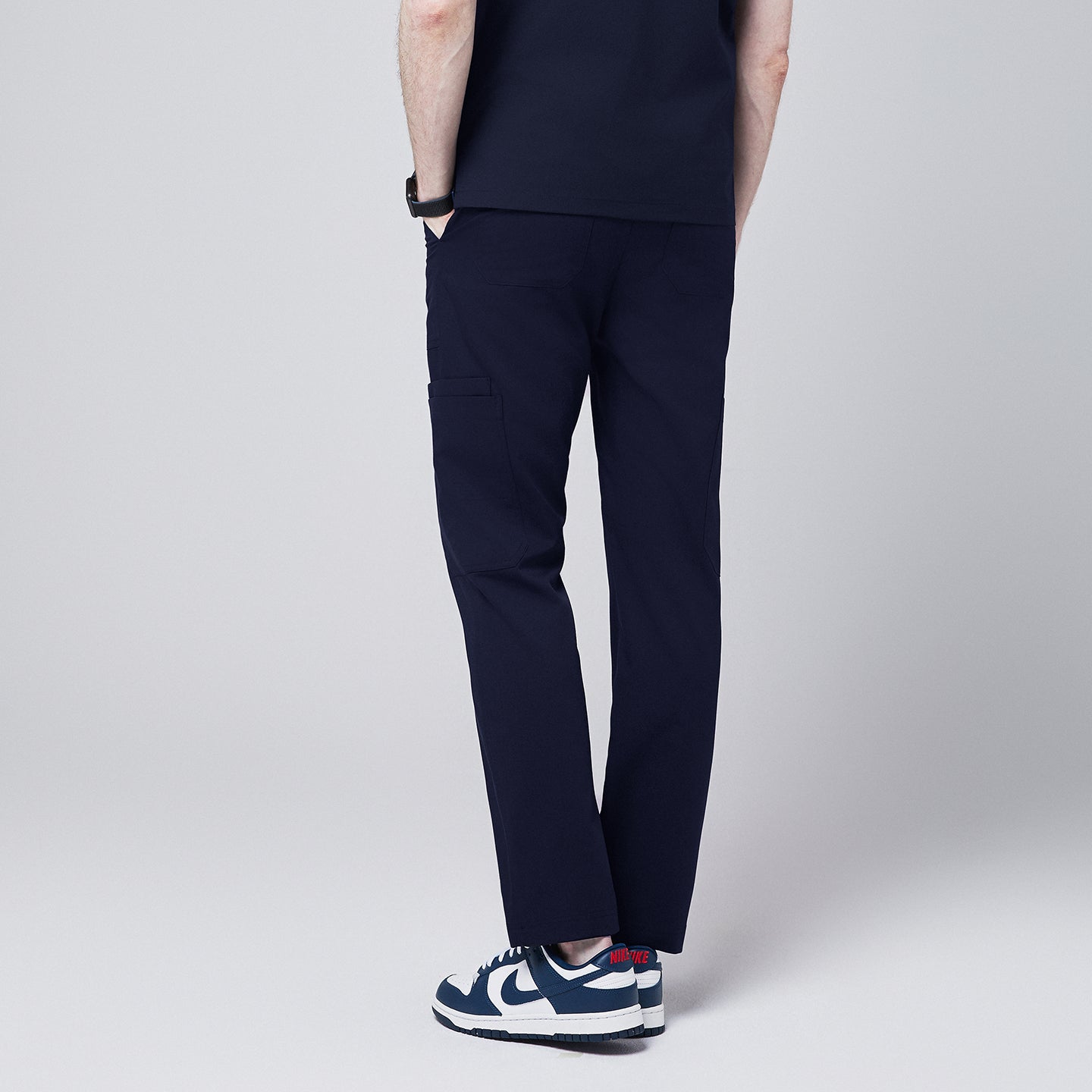 man wearing Zenir navy 8-pocket straight scrub pants, rear view showcasing pocket details, paired with blue and white sneakers,Navy