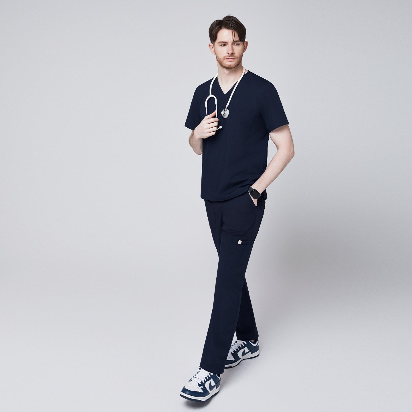 man wearing Zenir navy 8-pocket straight scrub pants and matching navy scrub top, holding a white stethoscope, paired with blue and white sneakers, walking confidently,Navy