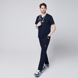 Image of man wearing Zenir navy 8-pocket straight scrub pants and matching navy scrub top, holding a white stethoscope, paired with blue and white sneakers, walking confidently,Navy