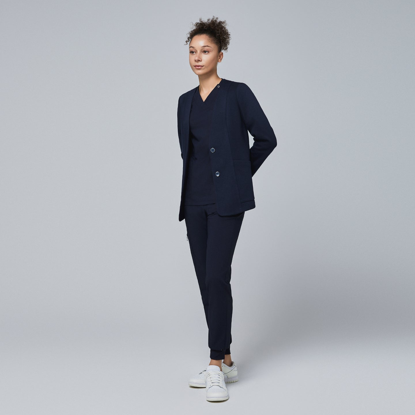 Professional woman modeling a navy comfort cardigan paired with a V-neck scrub top and jogger-style scrub pants, complemented by white sneakers,Navy