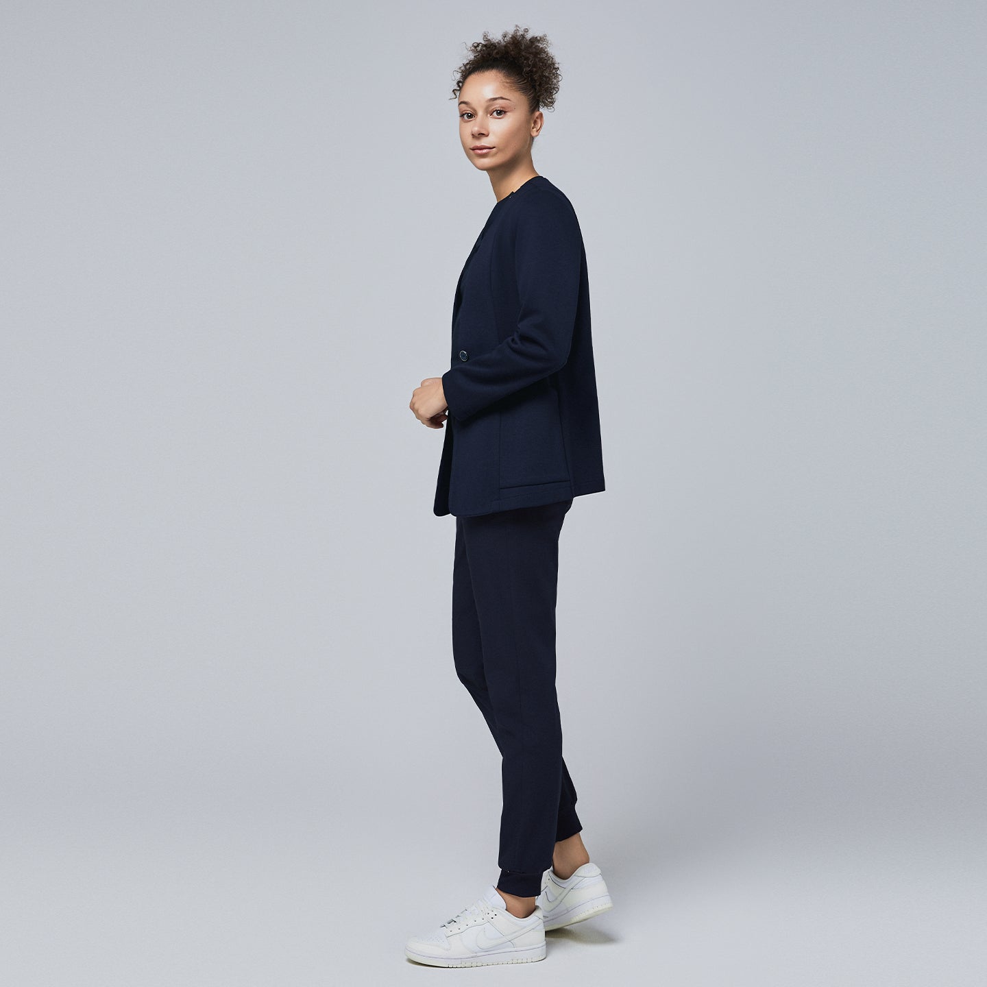 Side profile of a professional woman wearing a navy comfort cardigan layered over jogger-style scrub pants and a V-neck scrub top, styled with white sneakers,Navy