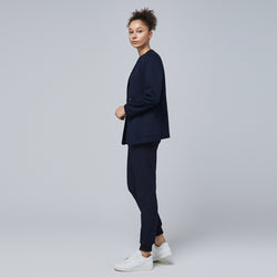 Image of Side profile of a professional woman wearing a navy comfort cardigan layered over jogger-style scrub pants and a V-neck scrub top, styled with white sneakers,Navy