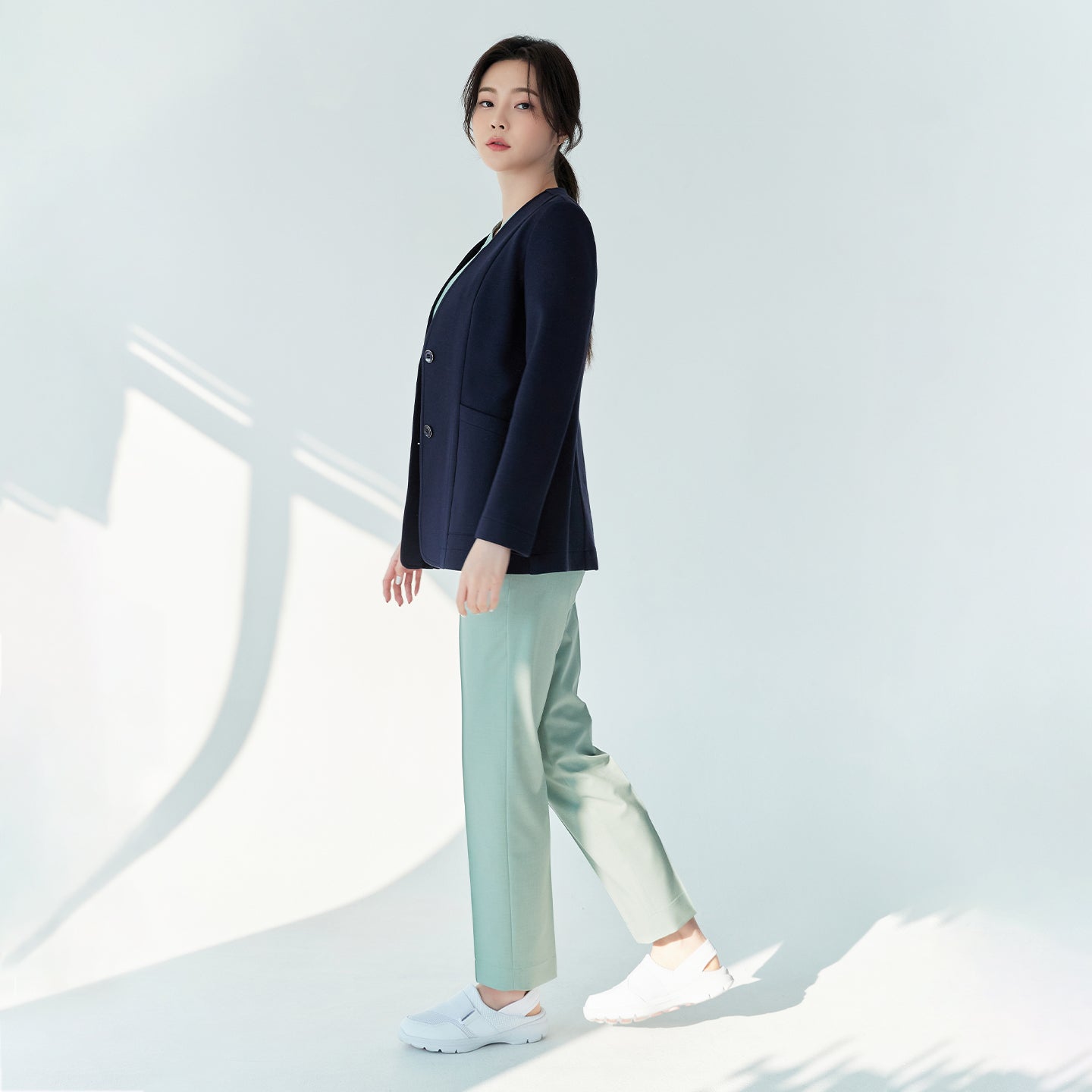 Woman in navy Zenir jacket over light green top and pants, standing and looking to the side, side view,Navy