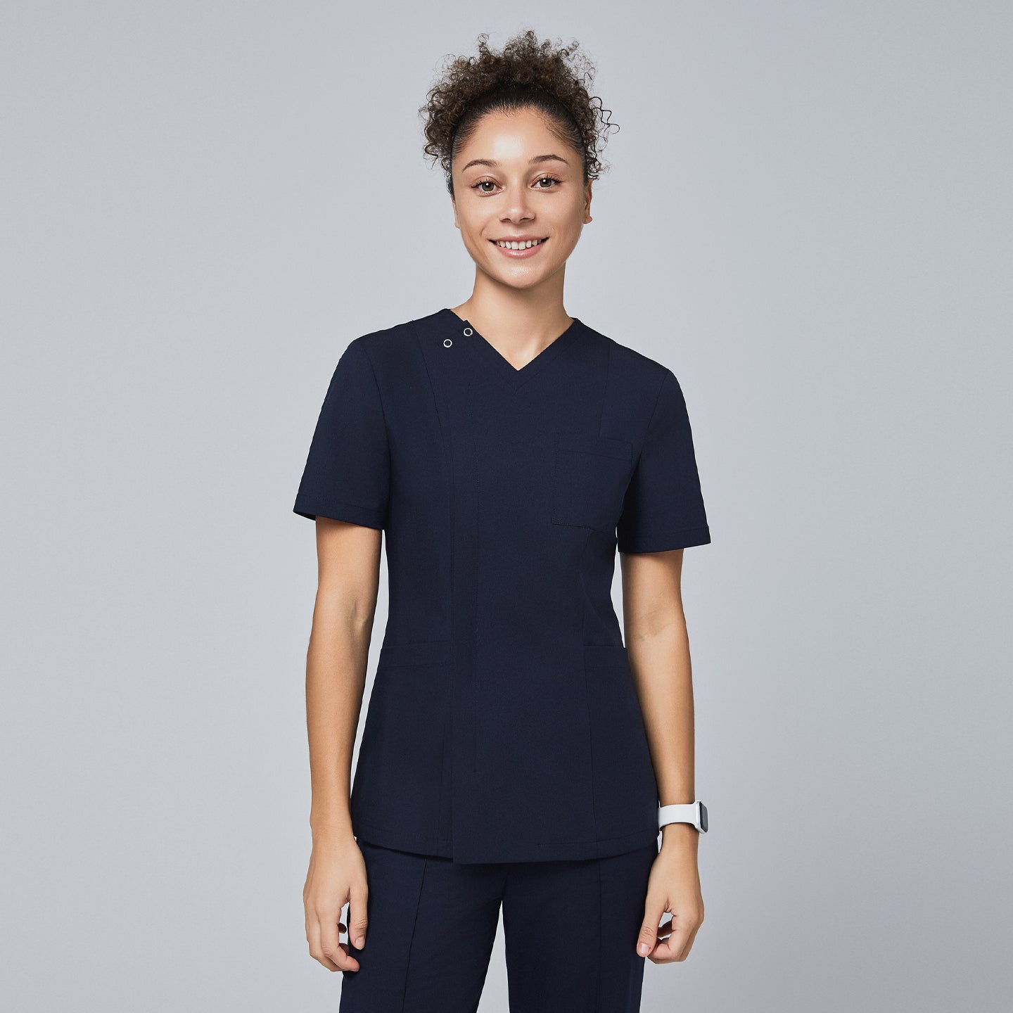 Female model wearing a navy V-neck scrub top with a subtle front zipper, short sleeves, chest pocket, and a fitted design, standing and smiling,Eco Navy