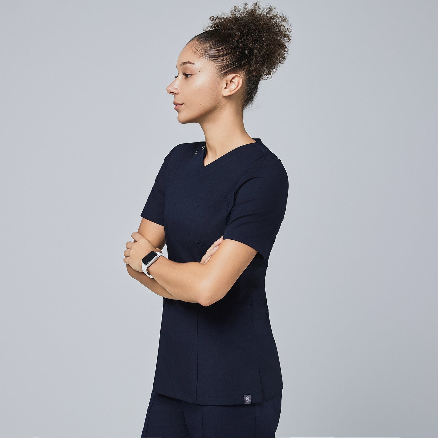 Female model wearing a navy V-neck scrub top with a front zipper and short sleeves, shown in a side profile with arms crossed,Eco Navy