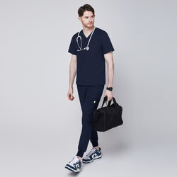 Image of Male healthcare professional wearing navy scrub top and jogger pants, carrying a black duffel bag with stethoscope around neck, looking to the side,Navy