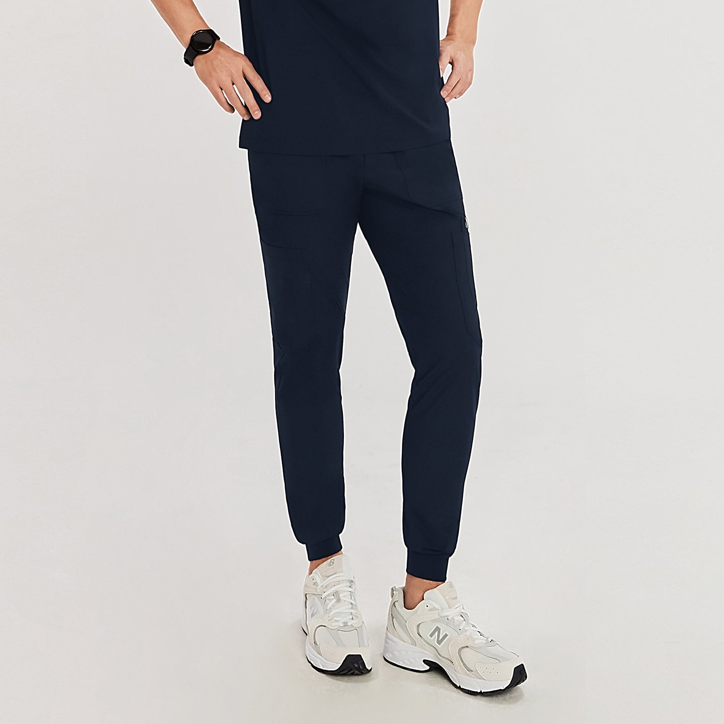 Close-up view of jogger-style scrub pants with elastic cuffs, showing a front pocket detail and white New Balance sneakers,Navy
