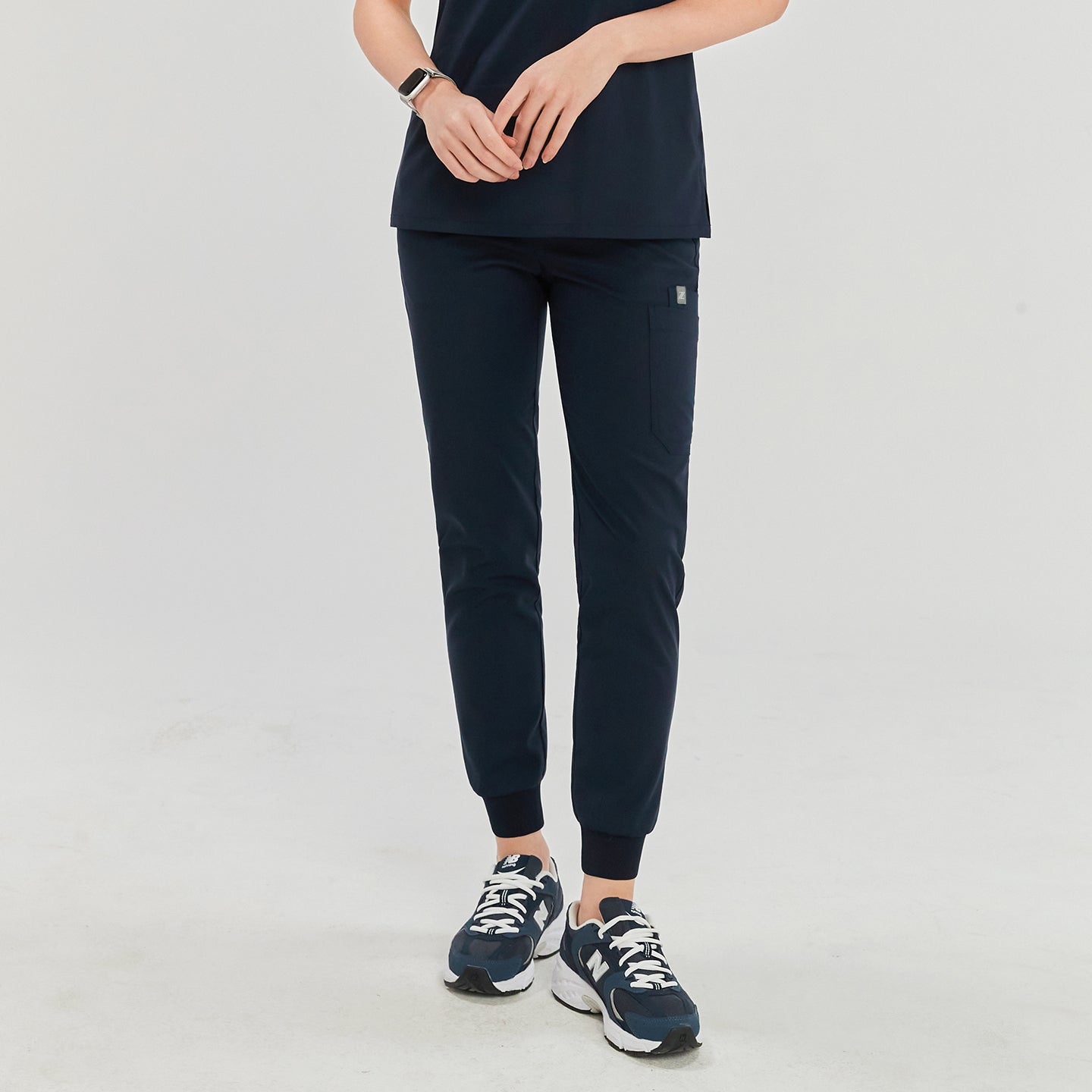 Woman in navy jogger scrub pants with ribbed cuffs and side pocket, paired with a matching scrub top and navy sneakers,Navy
