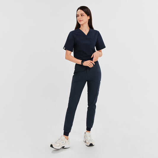Full-body view of a model wearing navy jogger scrub pants with a drawstring waist and side pockets, paired with a matching navy scrub top and white sneakers,Navy