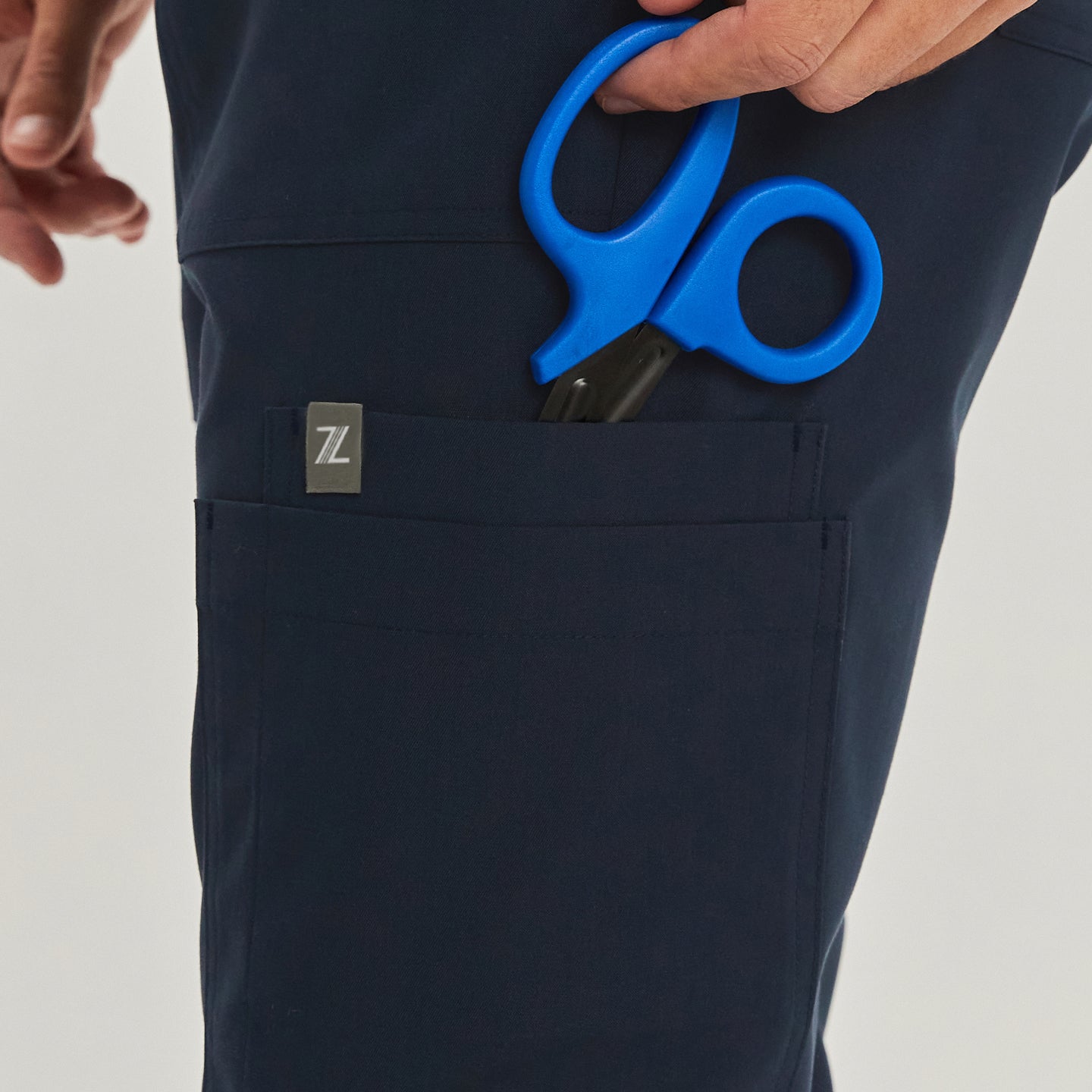 Jogger-style scrub pants with a front pocket holding blue medical scissors. The pocket features a small square logo tag,Navy