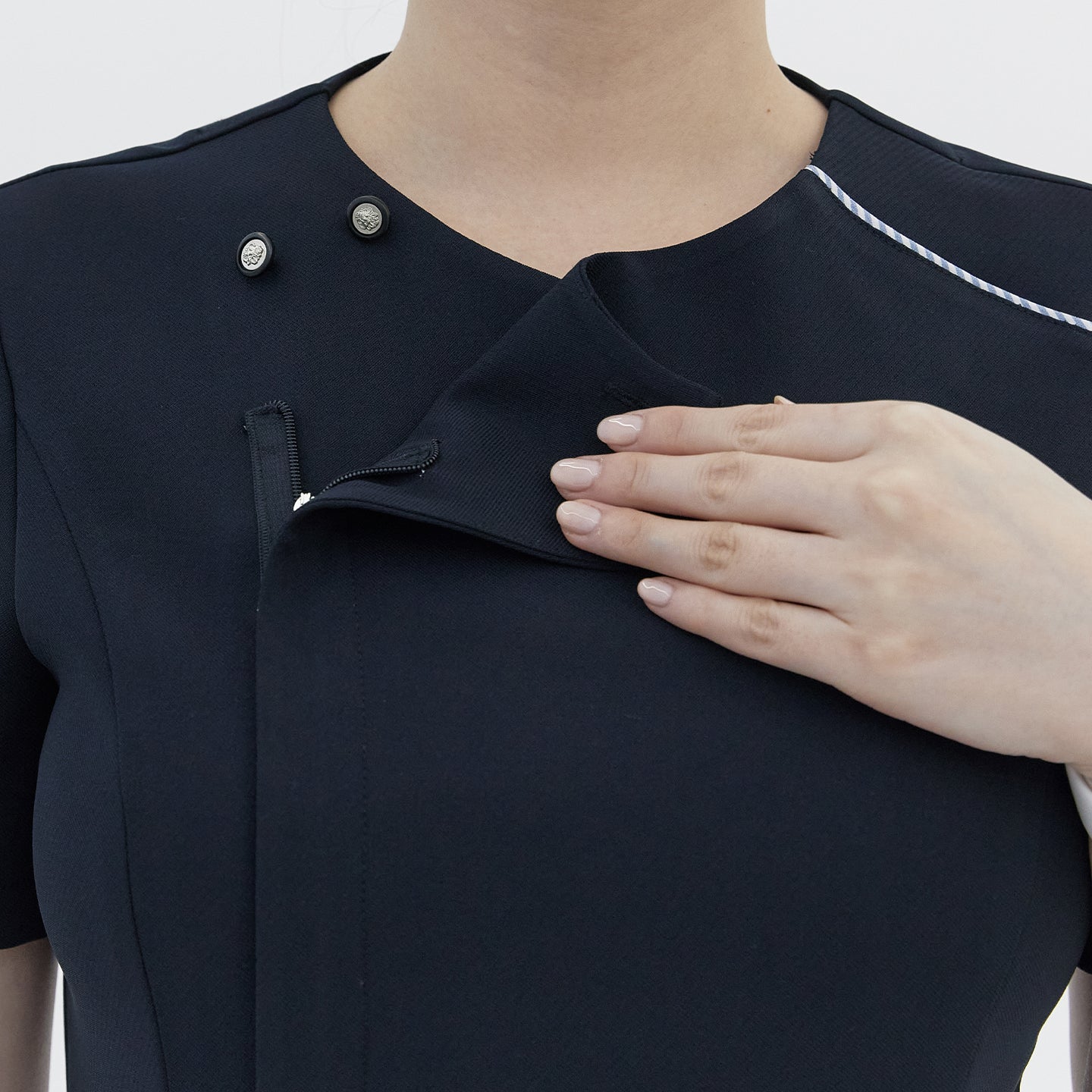 A close-up of a woman’s hand opening the front zipper of a navy round-neck top, revealing a hidden button detail and white trim,Navy