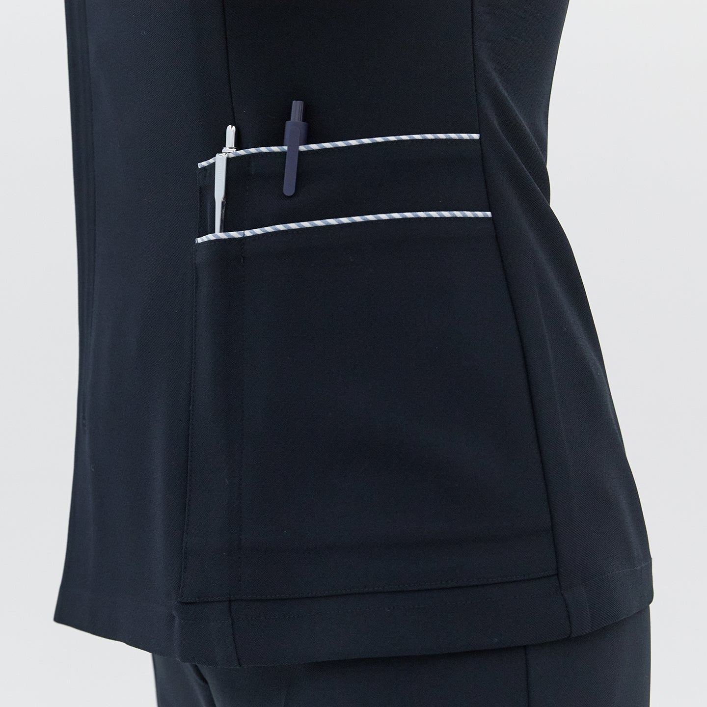  A detailed view of the side pocket on a navy round-neck top, featuring white trim and holding two pens,Navy