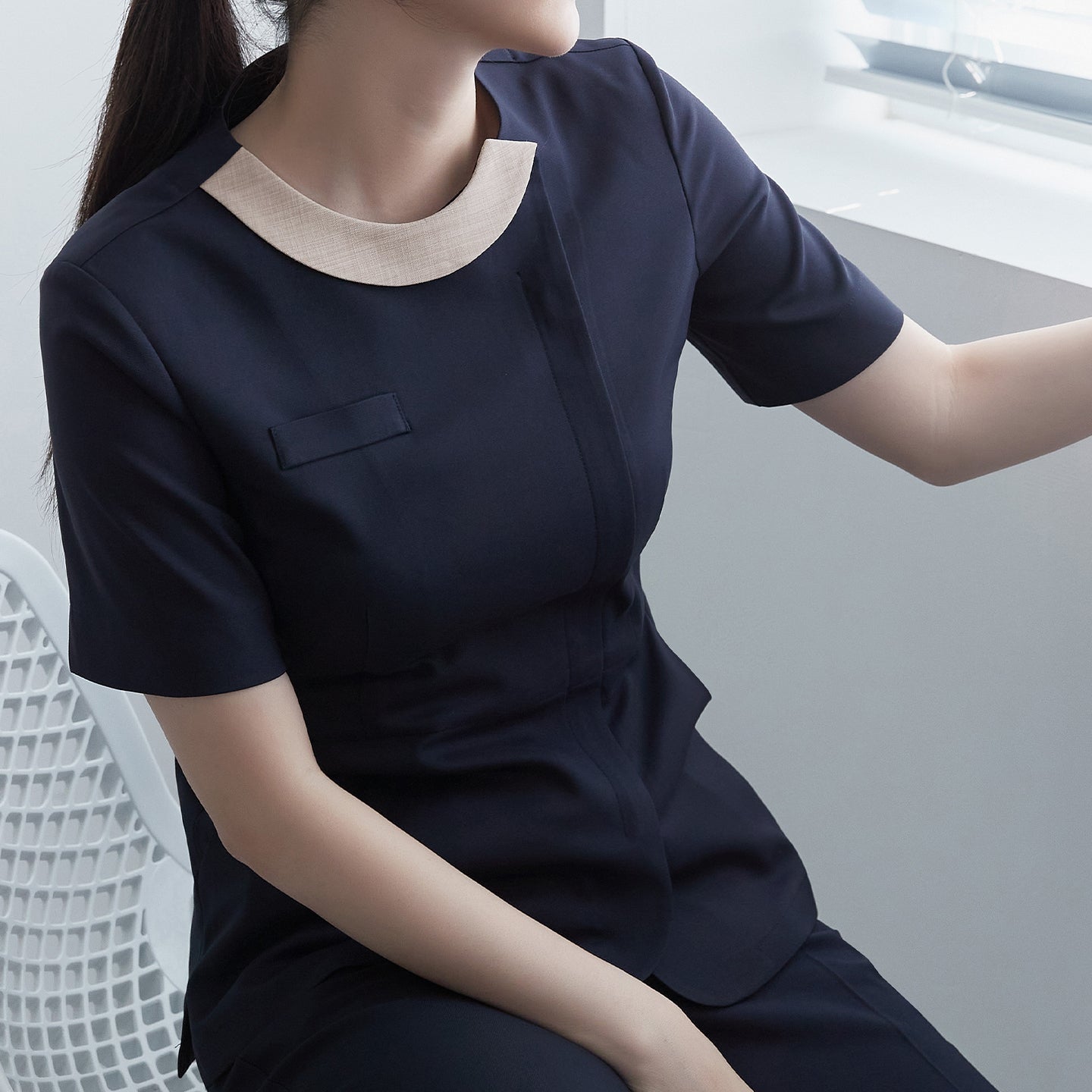 A woman wearing a navy round-neck front zipper top with a contrasting beige collar, sitting by a window,Navy