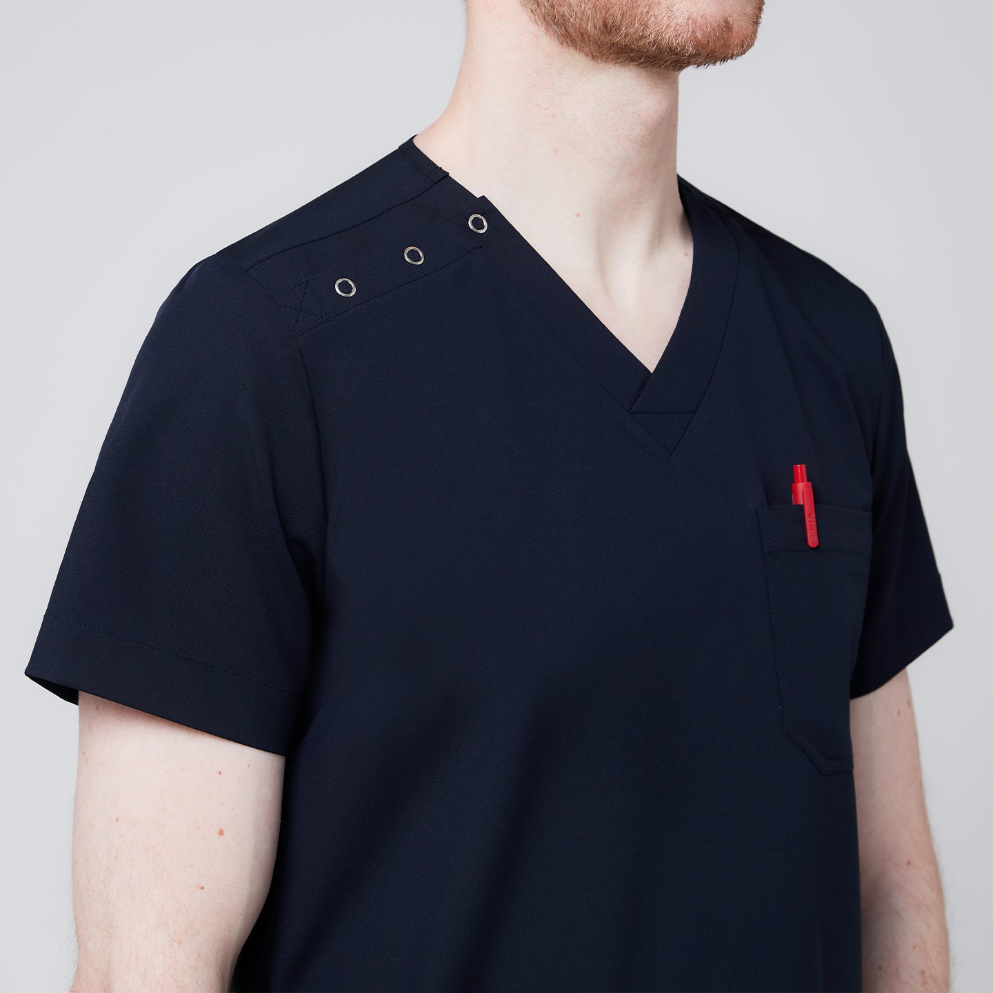 Close-up of a navy scrub top featuring button detailing on the shoulder and a chest pocket holding a red pen, highlighting the fine stitching and functional design,Eco Navy