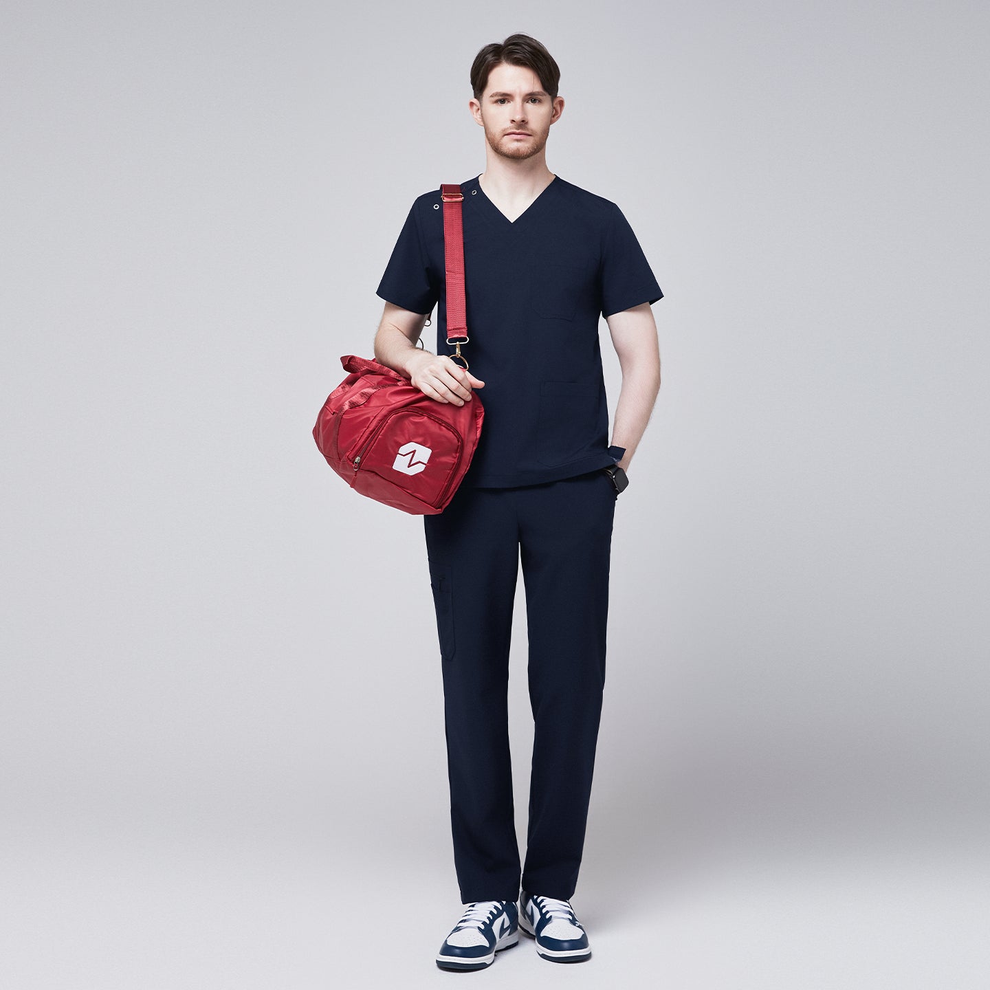 Man wearing a navy scrub set with a red duffel bag slung over his shoulder, highlighting the practicality and stylishness of the uniform for healthcare professionals,Eco Navy