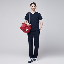 Image of Man wearing a navy scrub set with a red duffel bag slung over his shoulder, highlighting the practicality and stylishness of the uniform for healthcare professionals,Eco Navy