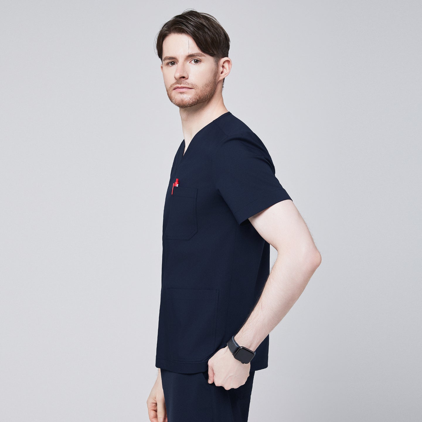 Side profile of a man wearing a navy scrub top with shoulder button detailing, showcasing a sleek and modern design with a red pen in the chest pocket,Eco Navy