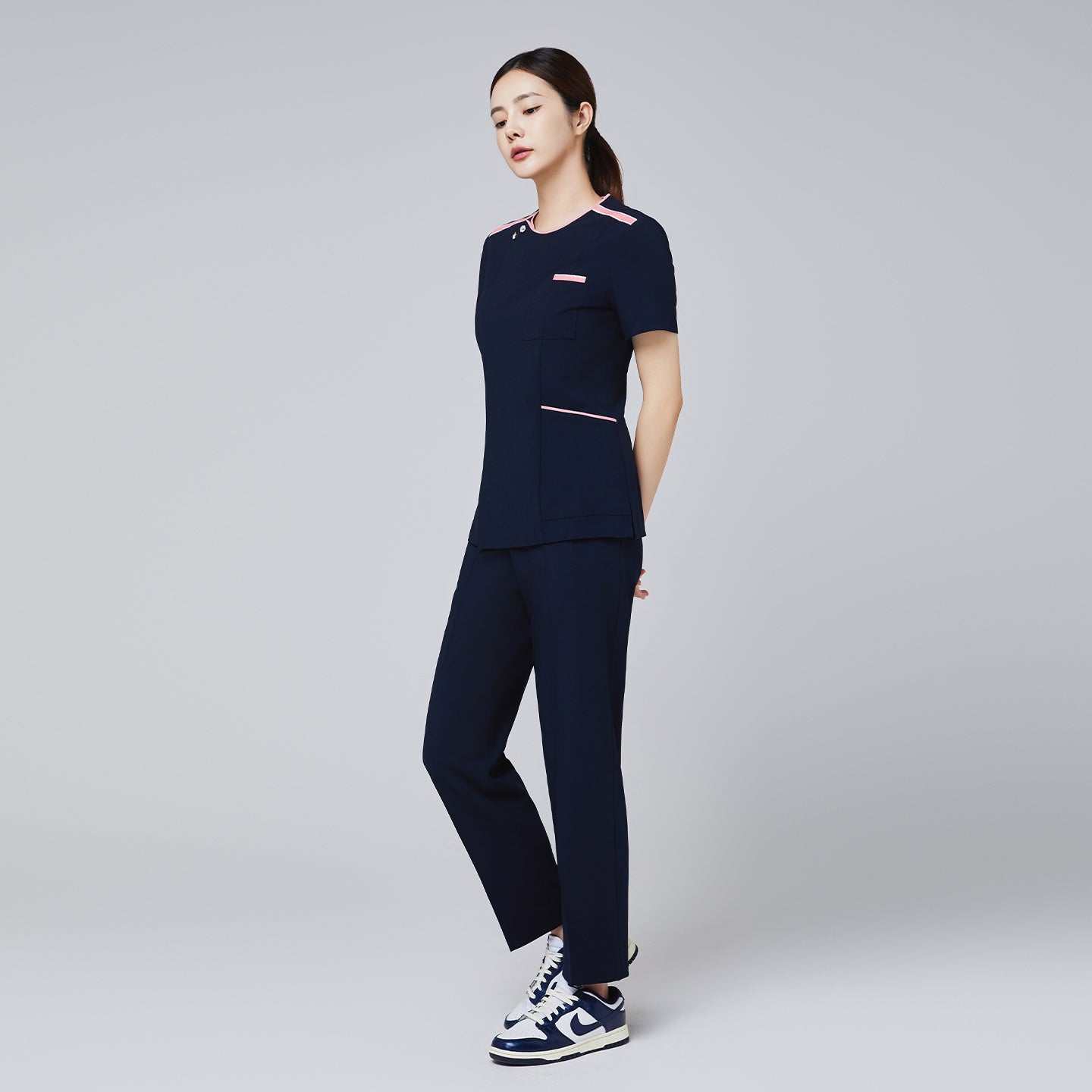 Full-body view of a woman wearing a navy scrub set with pink edge detailing, paired with casual sneakers,Navy