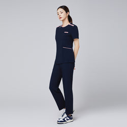 Image of Full-body view of a woman wearing a navy scrub set with pink edge detailing, paired with casual sneakers,Navy