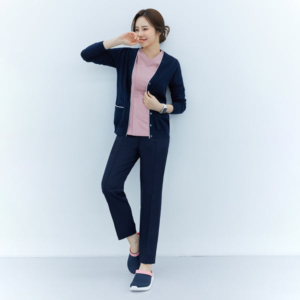Woman wearing a navy soft touch cardigan over a pink top and navy pants, leaning against a wall, smiling, with one hand on her hip and wearing slip-on shoes,Navy
