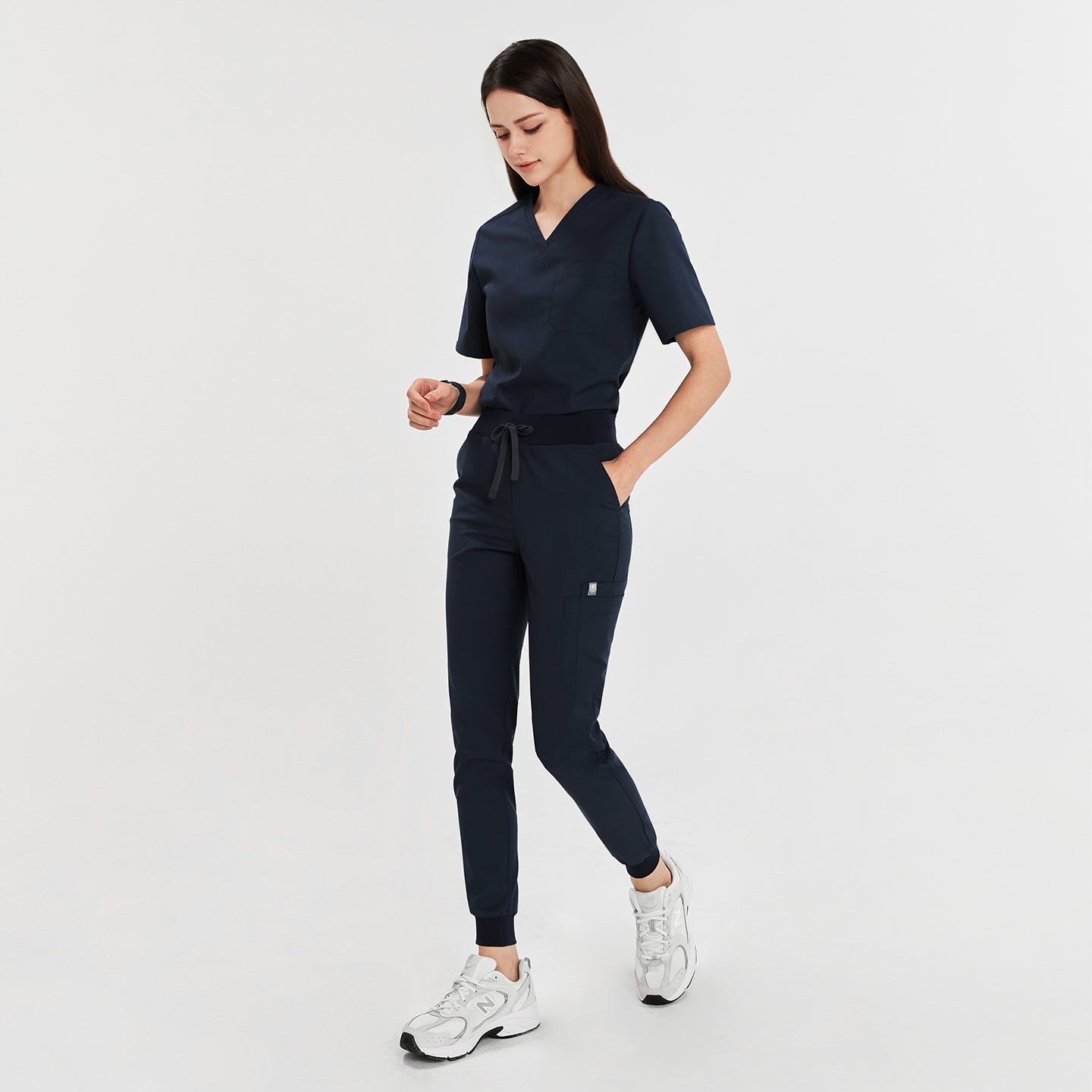 Woman wearing navy jogger scrub pants with waistband tie and side pocket, paired with white sneakers,Navy