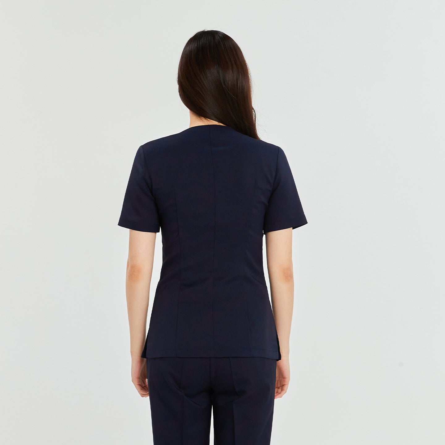 Woman in a navy front zipper scrub top with matching straight-leg pants, standing with her back to the camera,Navy
