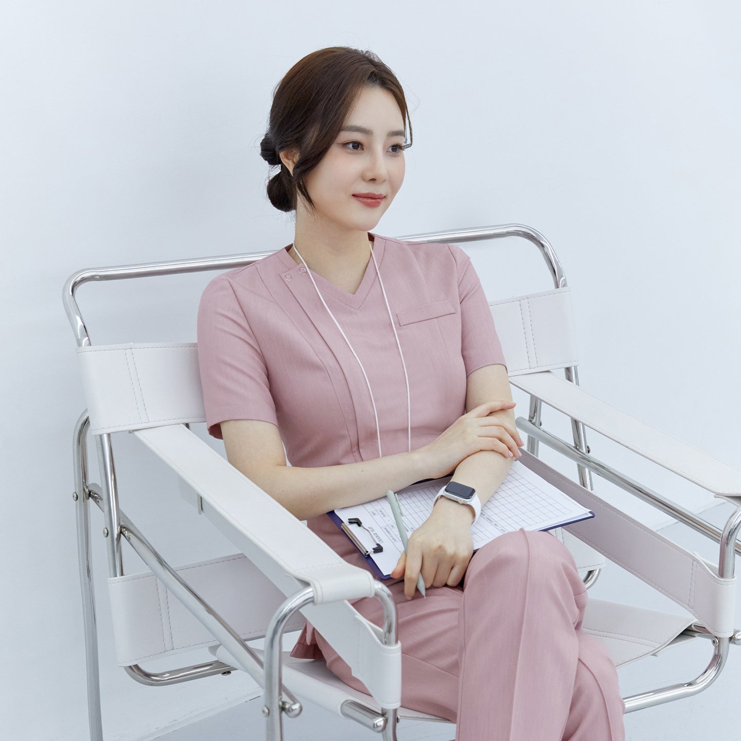 Woman sitting in a chair wearing a Zenir soft pink front zipper scrub top and matching pants,Soft Pink