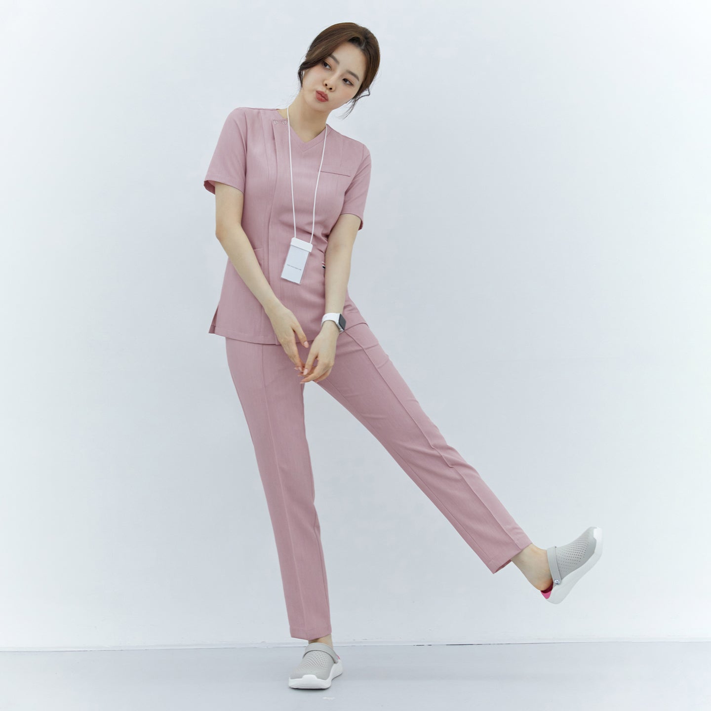 Woman in soft pink front zipper scrub top and straight-leg pants, standing with one leg slightly raised,Soft Pink