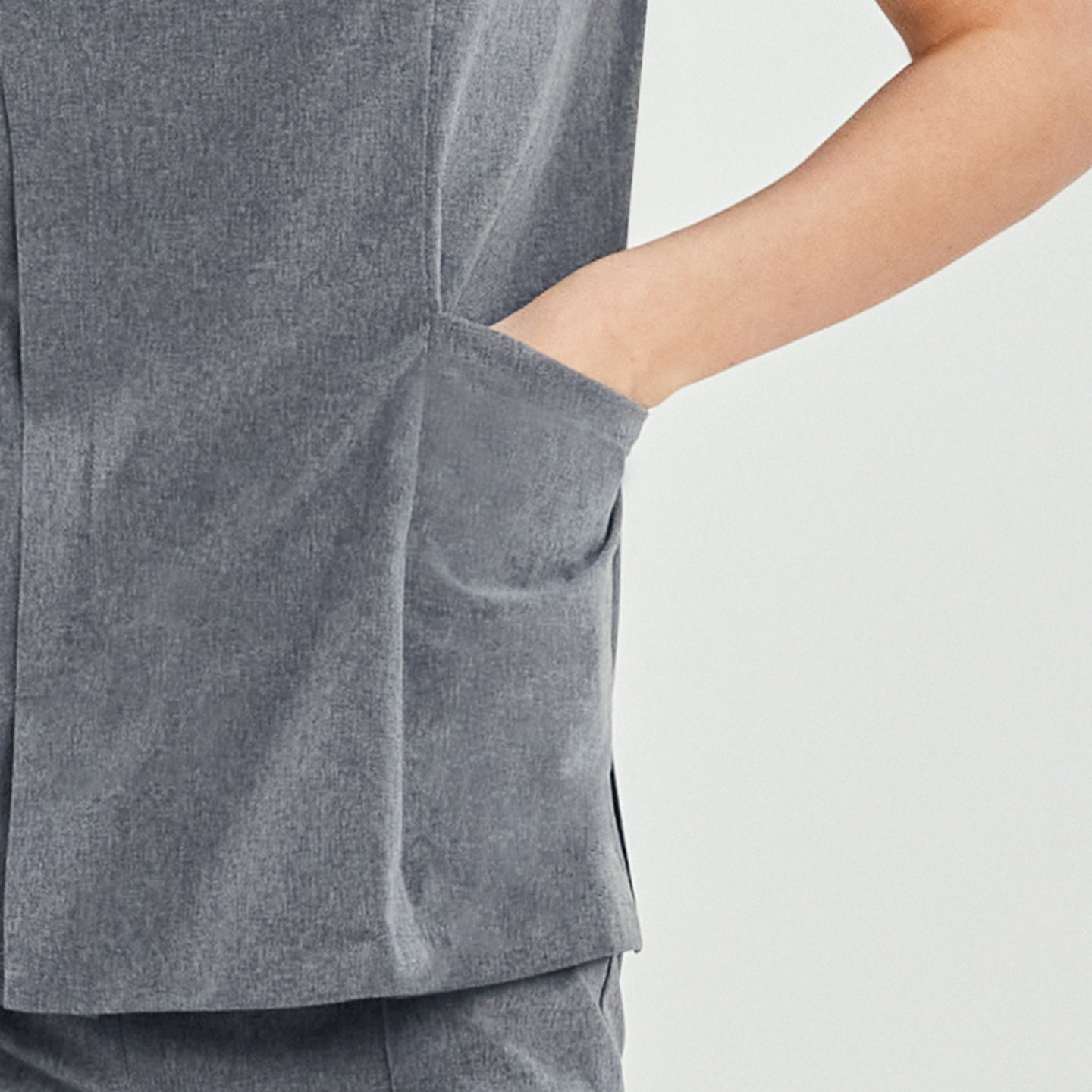 Close-up of the pocket detail on a soft gray Zenir front zipper scrub top, showing a hand in the pocket,Soft Gray