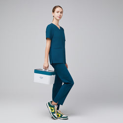 Image of Model in an ocean teal double pocket scrub top with matching scrub pants, green-yellow sneakers, and carrying a white medical kit,Ocean Teal