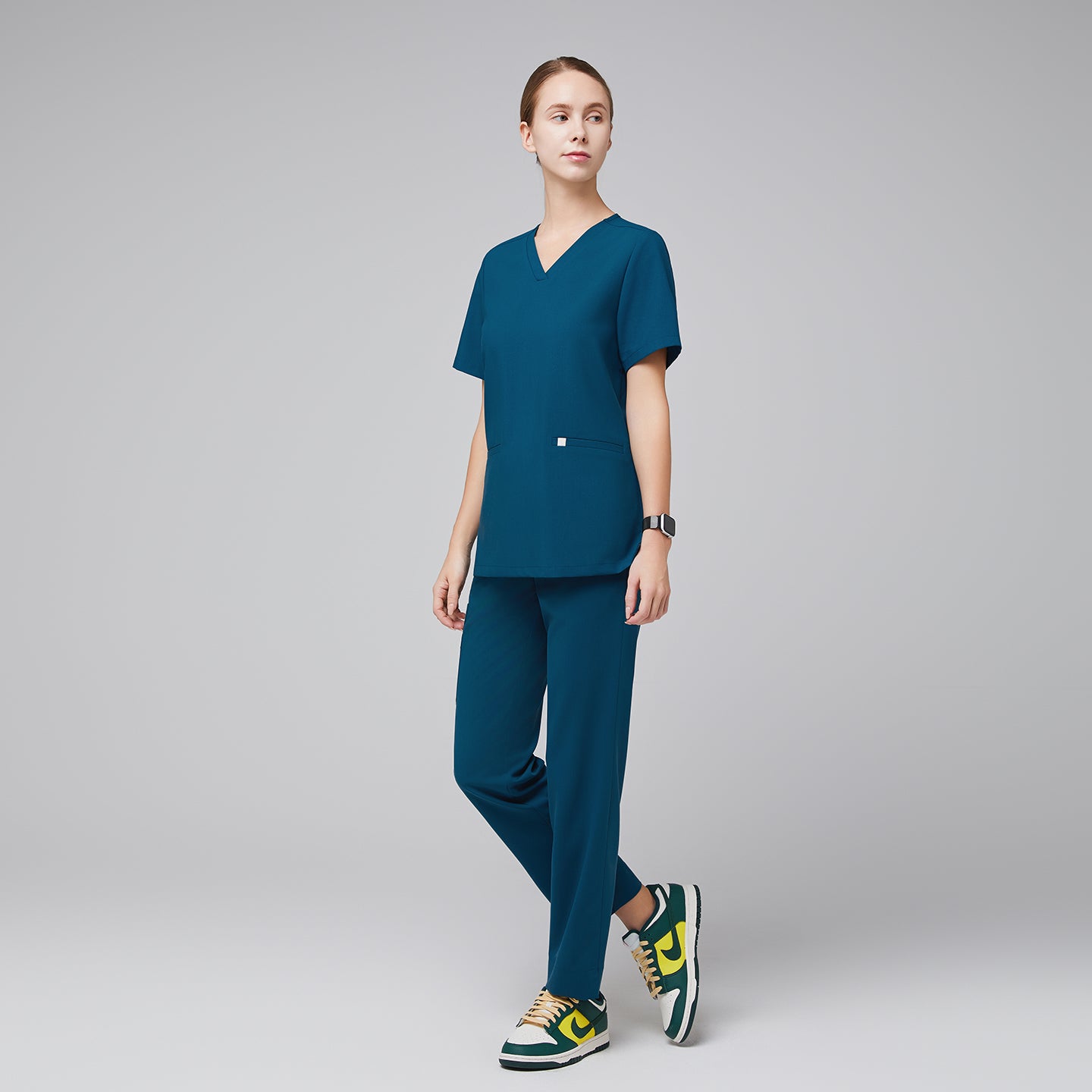 Model wearing an ocean teal double pocket scrub top with matching scrub pants and green-yellow sneakers,Ocean Teal