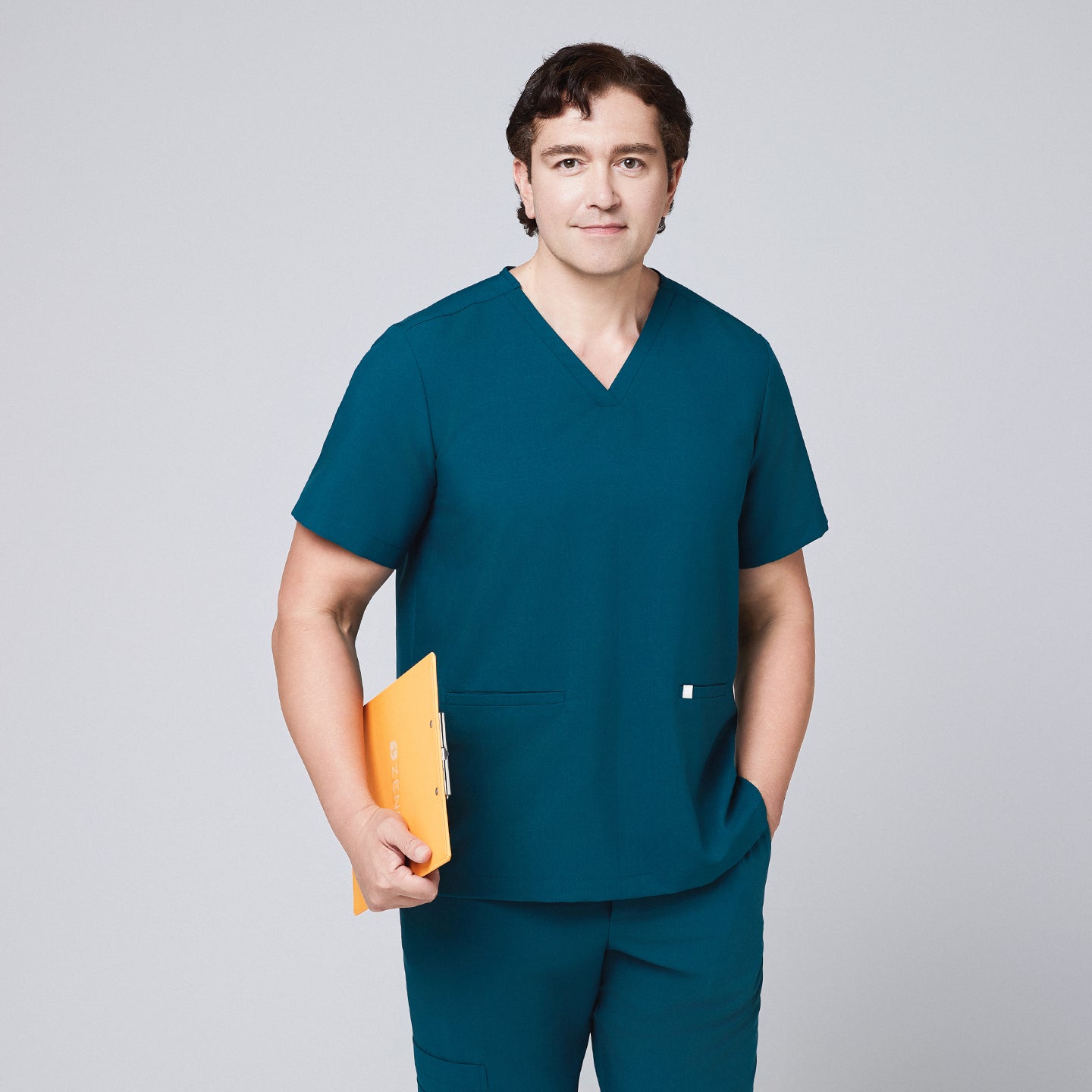 Man wearing an ocean teal scrub set with a double-pocket V-neck top, holding an orange clipboard,Ocean Teal