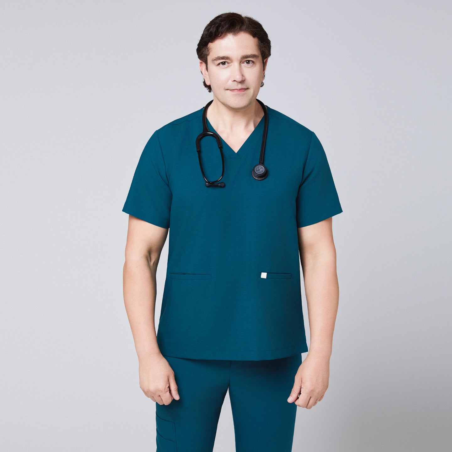 Man wearing an ocean teal scrub set with a double-pocket V-neck top, accessorized with a black stethoscope,Ocean Teal