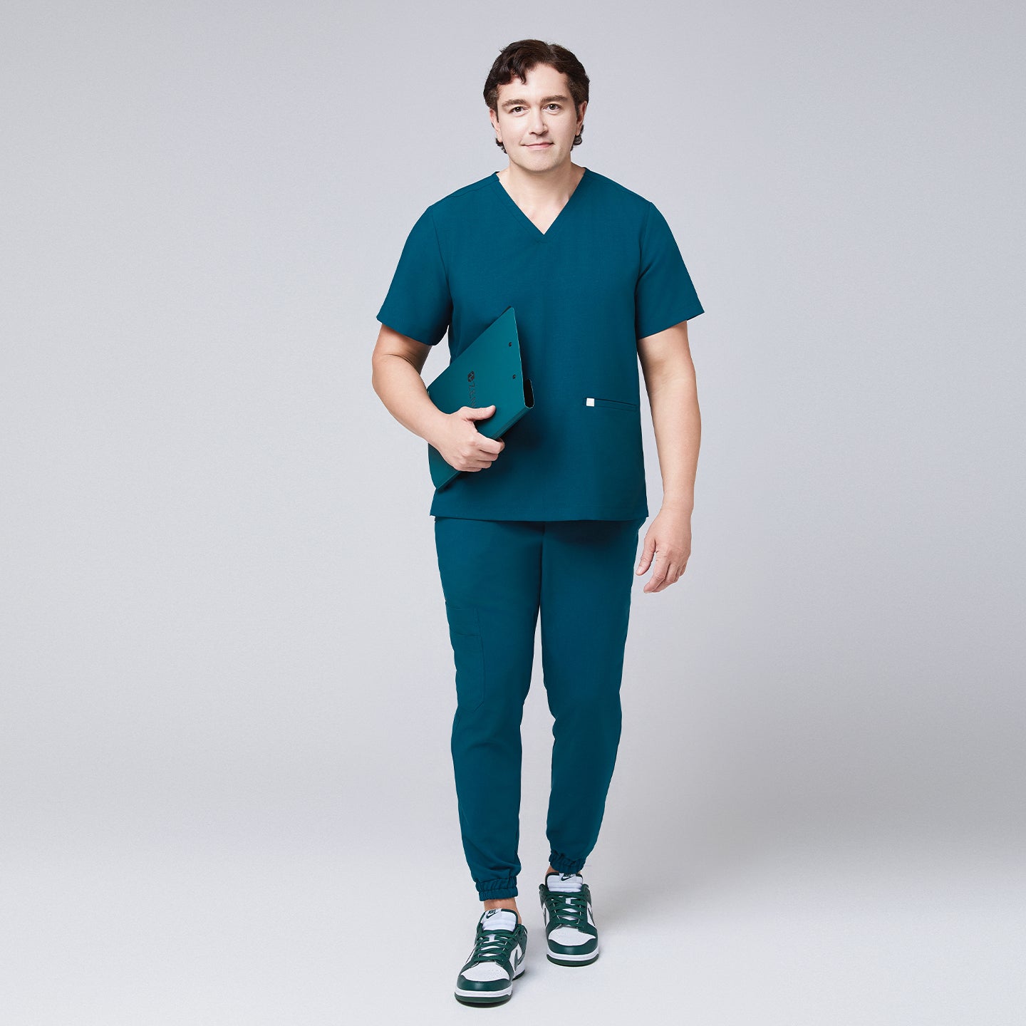 Full-body view of a man in an ocean teal scrub set with jogger pants and a double-pocket V-neck top, holding a teal folder,Ocean Teal