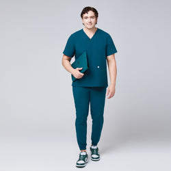 Image of Full-body view of a man in an ocean teal scrub set with jogger pants and a double-pocket V-neck top, holding a teal folder,Ocean Teal