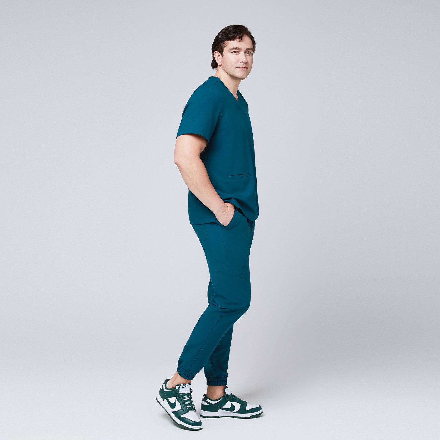 Side view of a man wearing an ocean teal scrub set with jogger pants and a double-pocket V-neck top,Ocean Teal