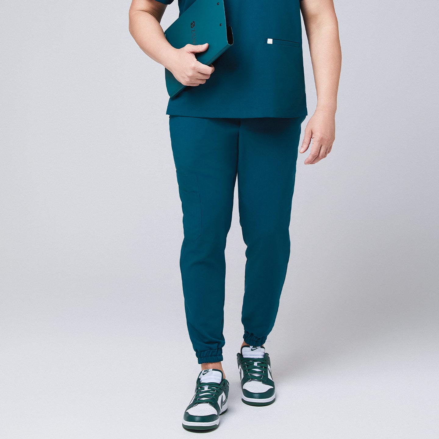 Front view of ocean teal jogger scrub pants with elastic cuffs and a cargo pocket, paired with green and white Nike sneakers,Ocean Teal 