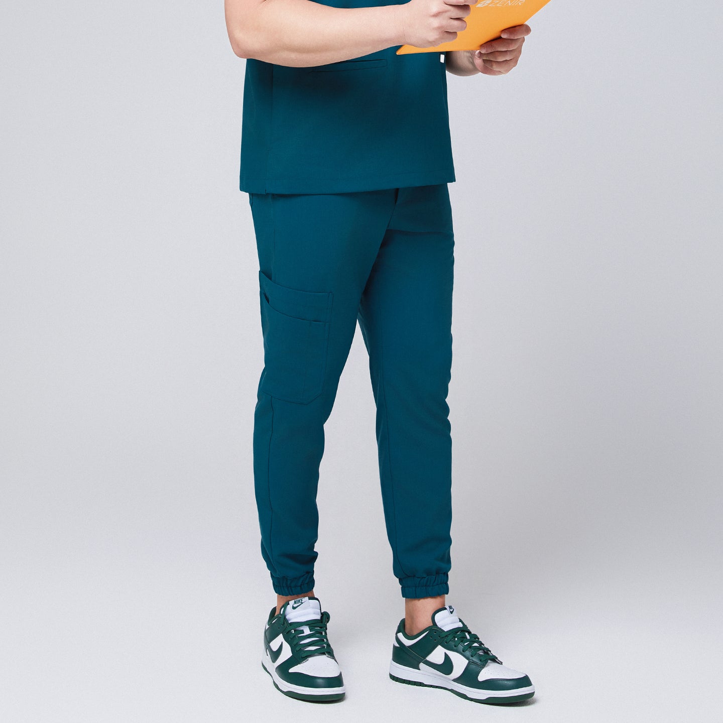 Side view of ocean teal jogger scrub pants with a cargo pocket and elastic cuffs, paired with green and white Nike sneakers,Ocean Teal 