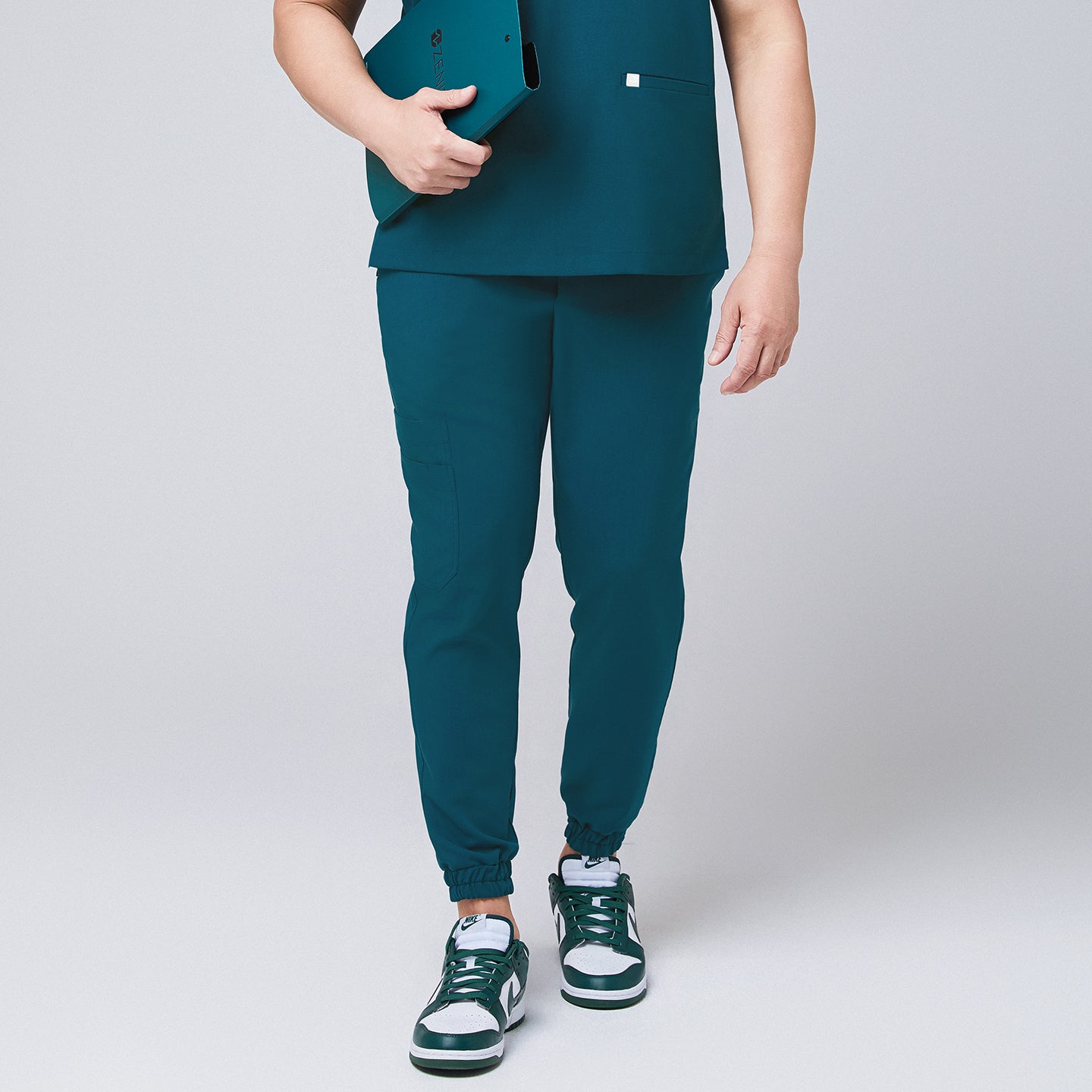 Ocean teal jogger scrub pants made of stretchy fabric and matching ocean teal scrub top, with a teal binder in hand,Ocean teal