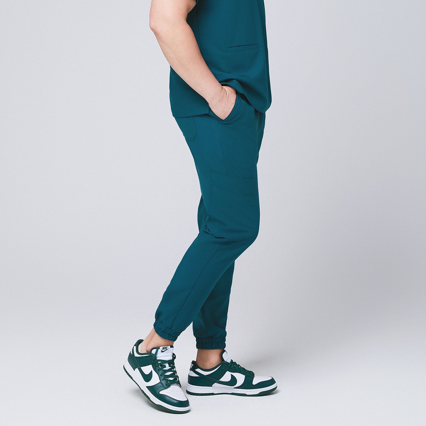 Ocean teal jogger scrub pants made of stretchy fabric and matching ocean teal scrub top, with teal sneakers and hands in pocket,Ocean teal