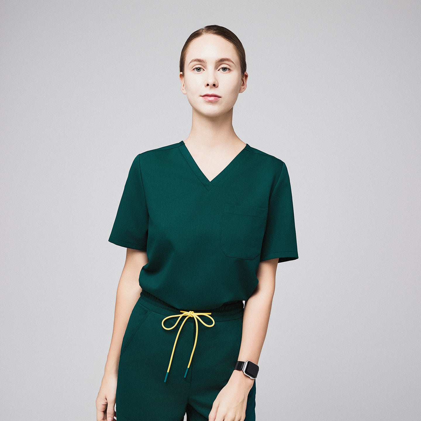 Woman wearing a pine green scrub top with a front pocket, paired with matching pants and a yellow drawstring,Pine Green