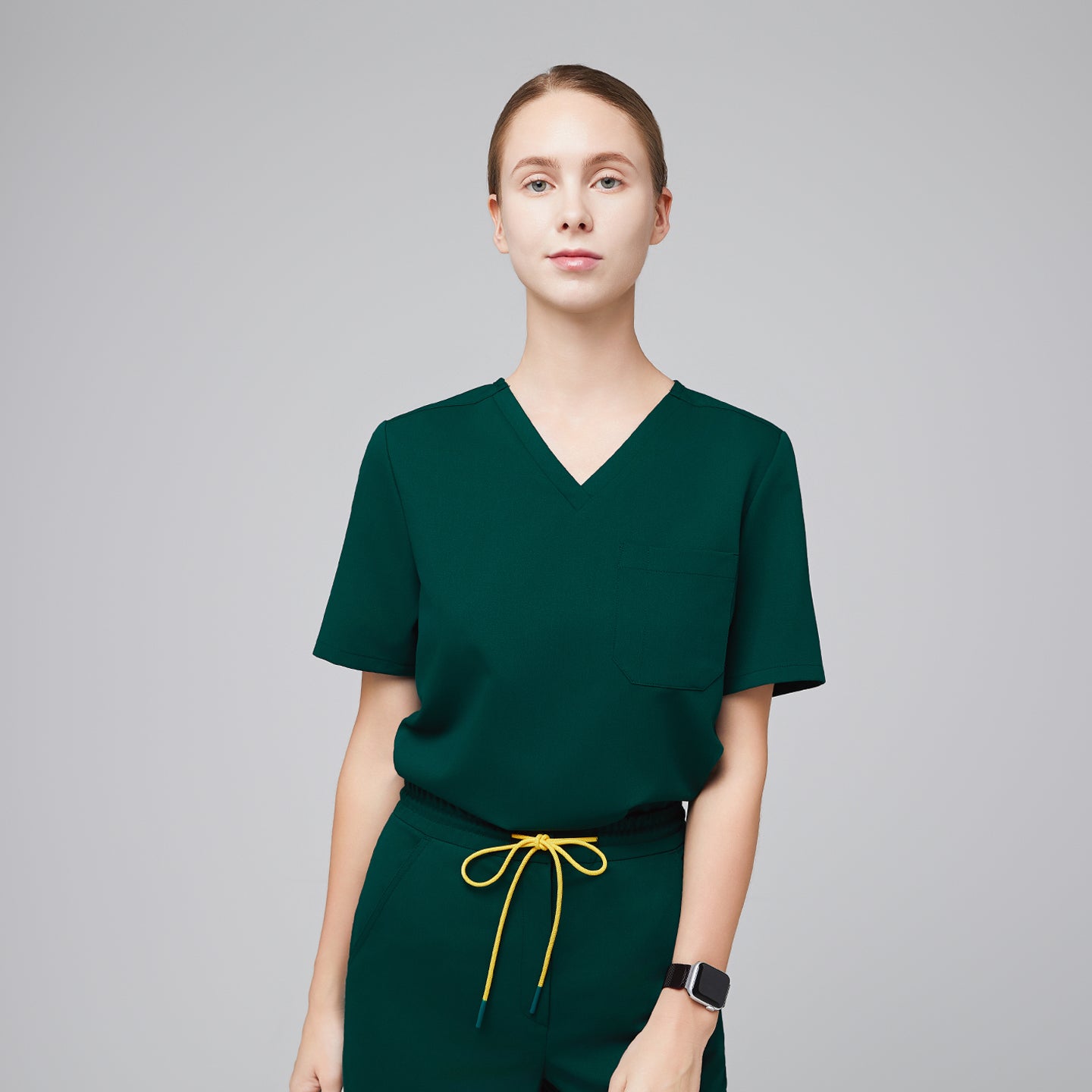 Woman wearing a pine green scrub top with a front pocket, paired with matching pants and a yellow drawstring,Pine Green