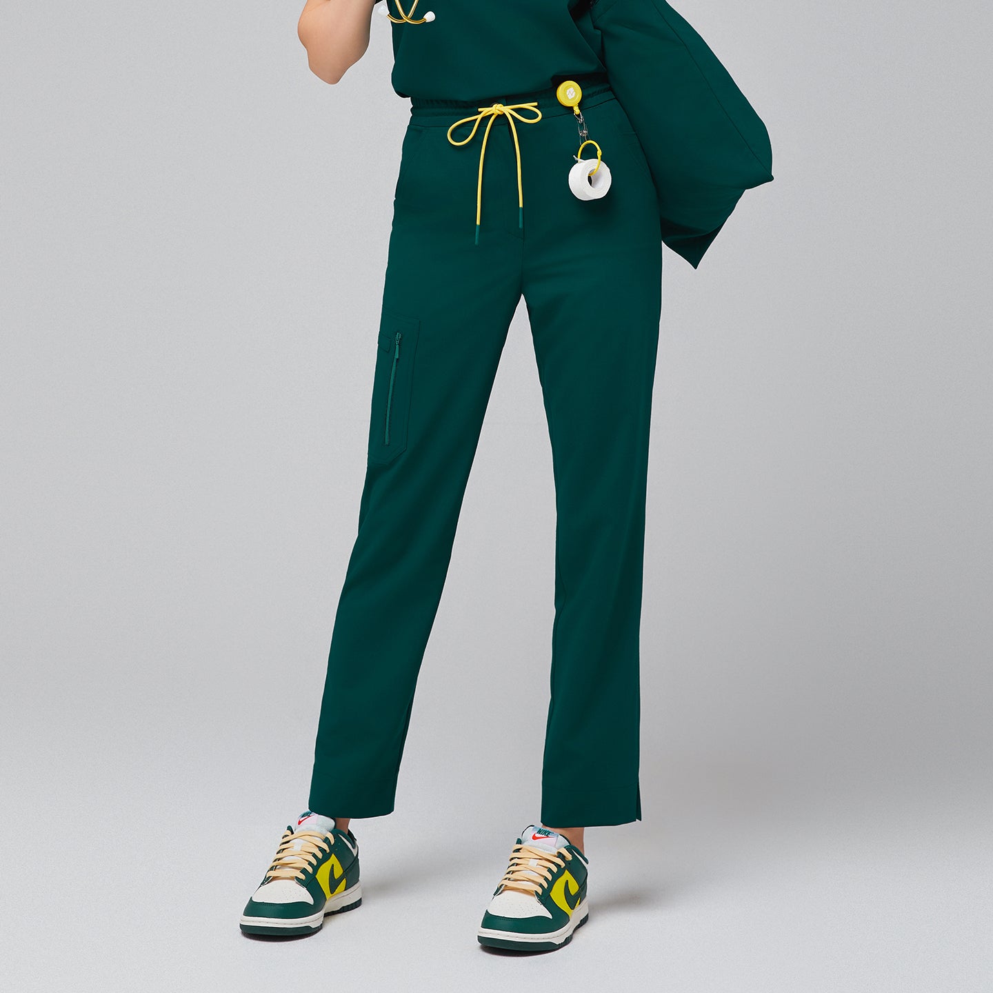 Scrub pants featuring a drawstring waist, zipper pockets, and split hem, paired with colorful sneakers and accessorized with a stethoscope and ID badge for a functional professional look,Pine Green