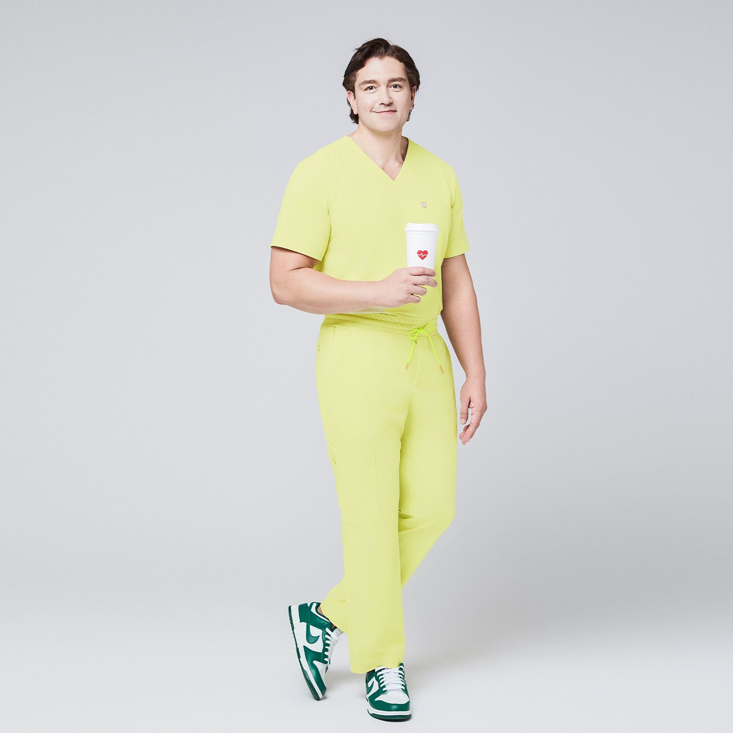 Full-body view of a model wearing pineapple yellow scrub pants paired with a matching top, holding a cup and standing confidently,Pineapple Yellow